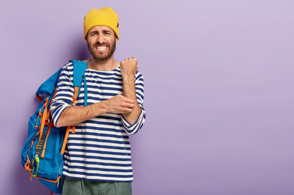 displeased man scratches itch hand suffers from dermatology problem dressed casual clothes has travel with tourist backpack clenches teeth isolated purple background copy space area