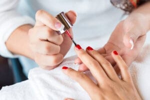 professional manicurist applying red nail polish to clients hands