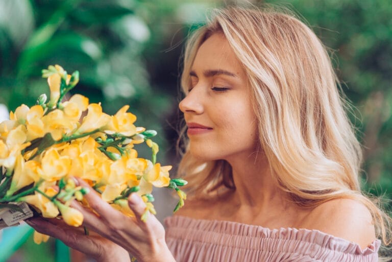 close up blonde young woman smelling freesia flowers