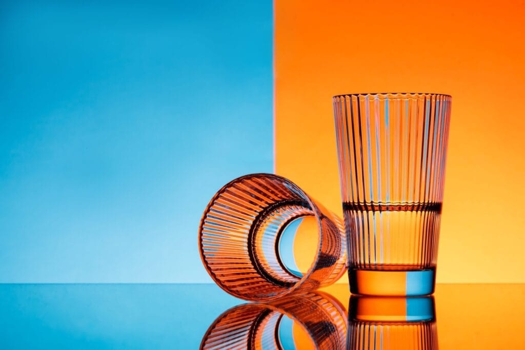 two glasses with water over blue and orange background.