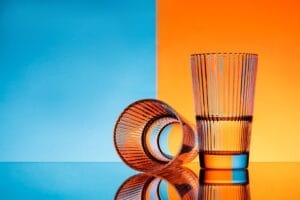 two glasses with water over blue and orange background.